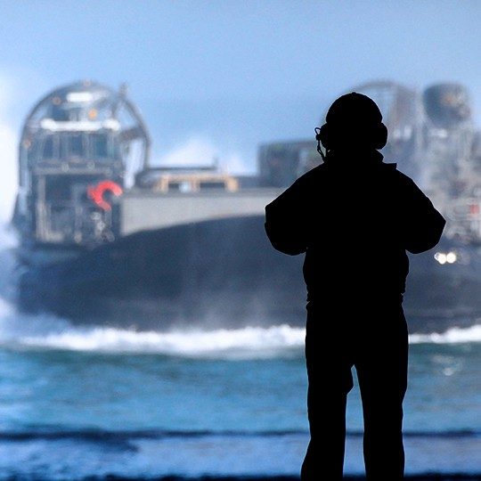 Silhouette of a sailor with a headset using maritime communications to communicate with a LCACs out at sea 