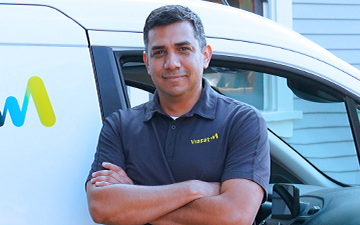 A Viasat installer stands in front of a white Viasat van with his arms crossed